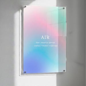 May include: A framed art print with a soft, colorful gradient of pink, blue, and green hues. The word "AIR" is centered, with supporting text below. The artwork is mounted on a white wall.