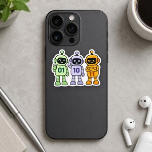 May include: A black smartphone featuring a sticker of three cartoon robots in green, purple, and orange. The green robot has the number 01, the purple robot has 10, and the orange robot has 11 printed on their chests. The robots have distinct expressions.