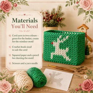 May include: A rectangular green crochet basket featuring a cream-coloured reindeer motif with a red nose. Beside it are two balls of yarn, a wooden crochet hook, a pair of scissors, a yarn needle, and a piece of squared paper with a reindeer chart.