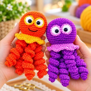 May include: Two crocheted octopus toys, one orange with a yellow collar and one purple with a pink collar. Both feature large white eyes with black pupils and multiple spiraled tentacles. The orange octopus has a stitched black smile.