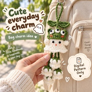 May include: A handmade crochet bag charm featuring a white ghost figure wearing a green frog hat with three eyes. The charm has a green loop for hanging and three dangling white flower-like shapes at the bottom. Text includes "Cute everyday charm", "Bag charm idea", "Add a little handmade happiness to your day", "Good Things Ahead", and "Digital Pattern Only".
