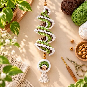 May include: A spiral-shaped crochet hanging ornament featuring alternating bands of dark brown, light green, and white yarn. The piece is accented with wooden beads and terminates in a circular crochet medallion with a tassel.