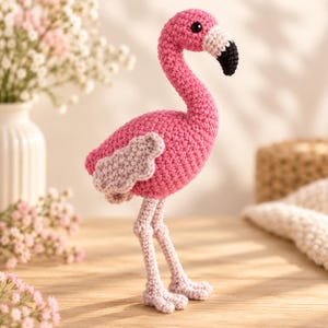 May include: A handcrafted crochet flamingo toy featuring a vibrant pink body, light pink wings, and long, slender light pink legs. The flamingo has a white beak base with a black tip and a small, round black eye, showcasing detailed yarn stitching.