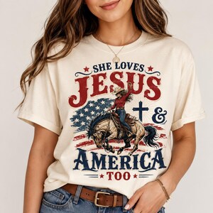 Peut inclure: Un t-shirt couleur crème avec une impression graphique portant le texte "SHE LOVES JESUS & AMERICA TOO". Le motif comprend un drapeau américain rouge, blanc et bleu en arrière-plan, une croix et l'illustration d'une cow-girl sur un cheval.