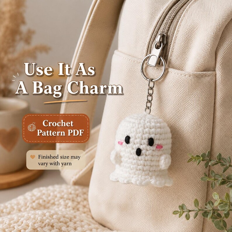 May include: A white crocheted ghost keychain attached to a beige canvas bag zipper. The ghost has black embroidered eyes, a black oval mouth, and small pink stitched cheeks. Text on the image reads: Use It As A Bag Charm, Crochet Pattern PDF.