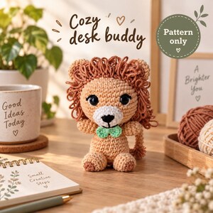 May include: A crocheted lion amigurumi toy with a tan body, a textured brown yarn mane, black safety eyes, a white muzzle, and a small mint green bow tie. The text "Cozy desk buddy" and "Pattern only" are visible in the image.