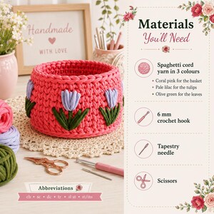 May include: A coral pink crocheted basket featuring pale lilac tulips and olive green leaves. The image includes a list of materials: spaghetti cord yarn, a 6 mm crochet hook, a tapestry needle, and scissors, alongside a list of abbreviations.