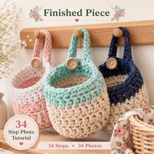 May include: Three hanging crochet baskets in light pink, mint green, and navy blue, each featuring a cream-colored base and a wooden button closure. The baskets are suspended from a wooden rack, with text reading Finished Piece and 34 Step Photo Tutorial.
