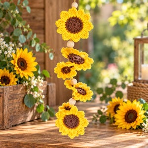 Puede incluir: Una decoraci&oacute;n colgante vertical que presenta cinco girasoles de ganchillo con p&eacute;talos de color amarillo brillante y centros de color marr&oacute;n oscuro, separados por cuentas de madera claras, redondas y lisas en un cord&oacute;n.