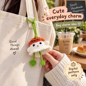 May include: A cream-colored canvas tote bag with the text Good Things Ahead and a heart symbol, featuring a crocheted ghost charm with an orange pumpkin hat, black eyes, and two green leaf-shaped dangling feet attached by a green yarn loop.
