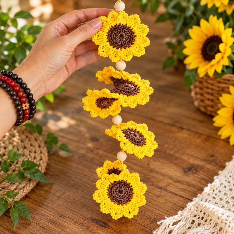 Puede incluir: Una decoraci&oacute;n colgante vertical que presenta cuatro girasoles de ganchillo con p&eacute;talos de color amarillo brillante y centros de color marr&oacute;n oscuro, separados por peque&ntilde;as cuentas de madera clara.