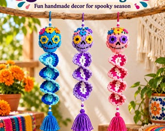 May include: Three crocheted skull ornaments hanging from a branch. Each skull features colorful floral accents and a spiral tail ending in a tassel. The blue, purple, and pink skulls are decorated with yarn flowers and stitched facial details.