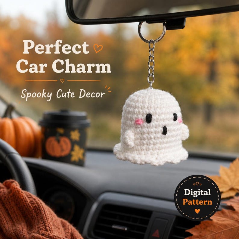 May include: A white crocheted ghost ornament hanging from a silver metal keychain. The ghost features small black circular eyes, a black oval mouth, and pink stitched cheeks. The text Perfect Car Charm Spooky Cute Decor and Digital Pattern is visible.