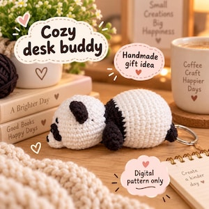 May include: A small, crocheted panda bear keychain featuring a white and black yarn body. The panda is lying down and includes a metal keyring attached to its back. The image contains text including "Cozy desk buddy," "Handmade gift idea," and "Digital pattern only."