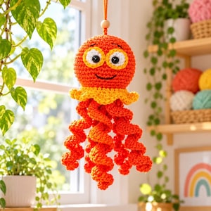 May include: A crocheted orange octopus hanging ornament with a round head, large white and yellow eyes, a black stitched smile, and a yellow ruffled collar. The body features multiple long, spiraling orange tentacles hanging downward.