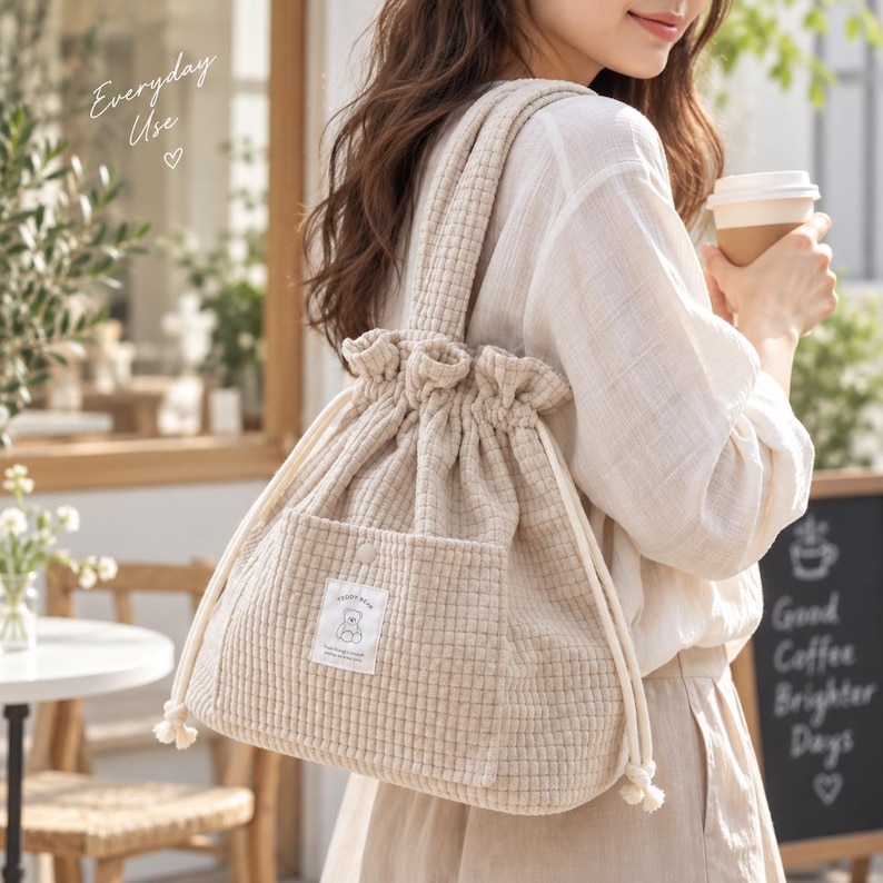 Peut inclure: Un sac &agrave; cordon de serrage beige &agrave; texture gaufr&eacute;e avec une poche avant orn&eacute;e d'un petit &eacute;cusson rectangulaire repr&eacute;sentant un ours et le texte "TEDDY BEAR". Le sac poss&egrave;de des bretelles en tissu &eacute;pais et des cordons blancs en haut.