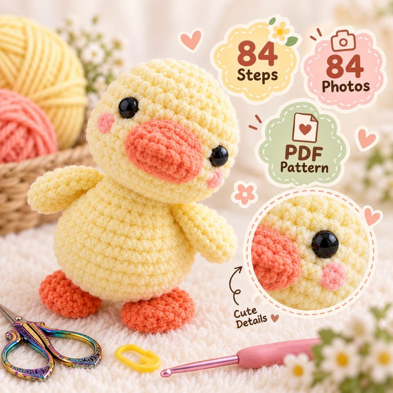 May include: A yellow crocheted duck toy with an orange beak and feet, black eyes, and pink cheeks. Text overlays include 84 Steps, 84 Photos, and PDF Pattern. A pink crochet hook, a yellow stitch marker, and iridescent scissors are visible.