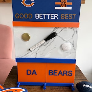 May include: A rectangular wall-mounted organizer featuring a blue and orange color scheme with the Chicago Bears logo, the text GSH, and the phrase GOOD BETTER BEST. The center section has a white marble pattern with a marker and two magnets.