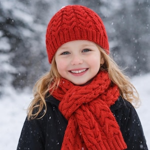 May include: A young person wearing a red knit hat and scarf, smiling in a snowy environment. The hat and scarf have a cable knit design. The person is wearing a black coat. Snowflakes are falling in the background.