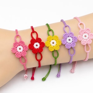 May include: Five adjustable bracelets featuring crocheted flower motifs in pink, red, yellow, purple, and light pink. Each flower has a white center and is attached to a thin cord with looped ends, creating a colorful set of floral wrist accessories.