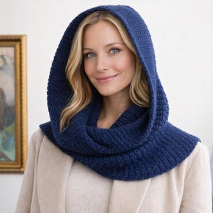 May include: A navy blue knitted hood and cowl. The hood covers the head, and the cowl wraps around the neck. The knitted fabric has a textured appearance. The garment is worn over a light-coloured coat. The hood and cowl are a single piece.