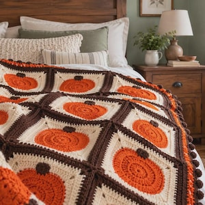 May include: A crochet blanket featuring a repeating square pattern, with each square displaying a textured orange pumpkin with a dark brown stem, framed by cream-colored yarn and joined together by thick, dark brown yarn borders.