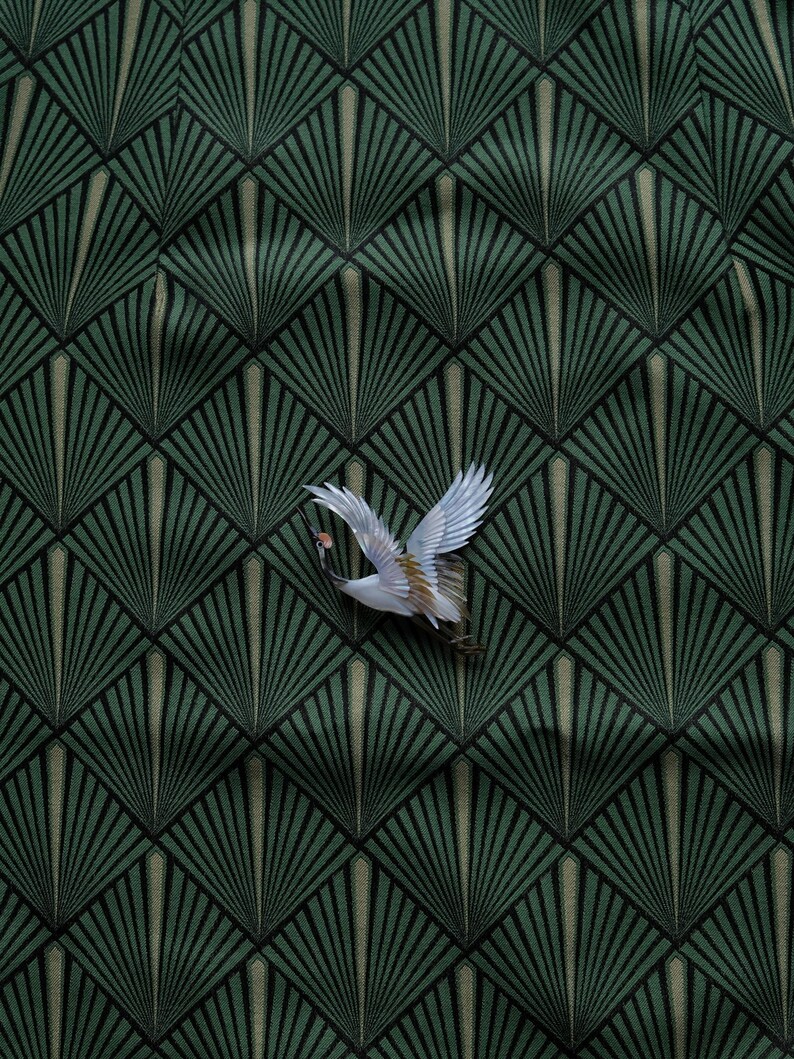 May include: A decorative fabric with a repeating geometric fan pattern in shades of green and black. A white and tan crane with outstretched wings is positioned in the upper right corner, adding a touch of nature to the design.