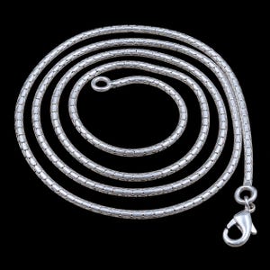 May include: A silver-toned snake chain necklace featuring a repeating textured pattern of small, rounded links. The chain is coiled in a circular shape and includes a polished lobster claw clasp at one end and a small circular jump ring at the other.