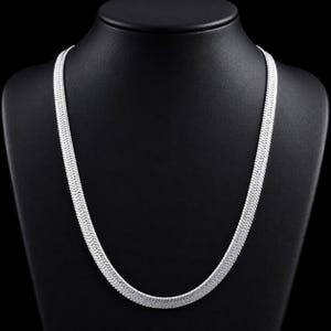 May include: A silver-toned herringbone chain necklace featuring a flat, flexible design with a tightly woven, multi-link pattern that creates a smooth, reflective surface. The necklace rests in a U-shape, showcasing a uniform width throughout.