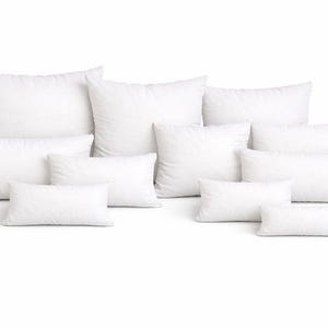 May include: A collection of white pillows in various sizes and shapes, including square and rectangular. The pillows are arranged on a white background, showcasing their fluffy appearance. Ideal for home decor and bedding.