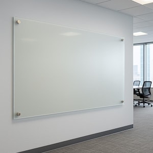 May include: A large, rectangular glass whiteboard mounted on a light gray wall. The whiteboard is secured with four silver-colored fasteners. The office setting includes a gray carpet and a view of a cityscape through a window.