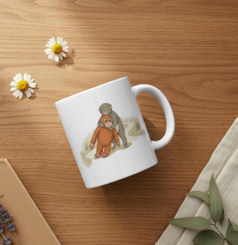 May include: White ceramic mug featuring a cartoon illustration of two orangutans. One orangutan is orange, and the other is gray. The mug has a curved handle and is set on a wooden surface with daisies.
