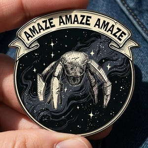 May include: A round, black and white enamel pin featuring a stylized insectoid creature against a starry night sky. The pin has the word "AMAZE" in a banner across the top. The design is detailed with fine lines and shading.