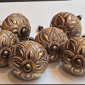 May include: A set of decorative cabinet knobs. The knobs are a warm, metallic brown colour with a floral design. Each knob has a central, circular accent and a screw for attachment.