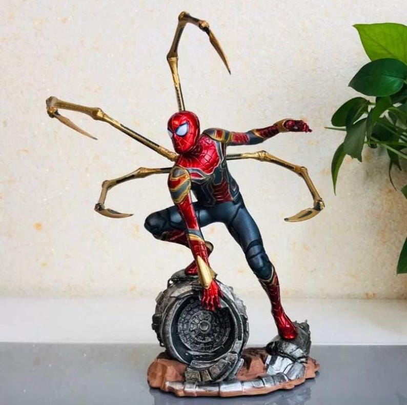 K&ouml;nnte beinhalten: Detaillierte Figur von Spider-Man in dynamischer Pose, mit rotem und goldenem Anzug und mehreren mechanischen Armen. Die Figur steht auf einem metallischen Sockel mit braunem und grauem Gel&auml;nde.