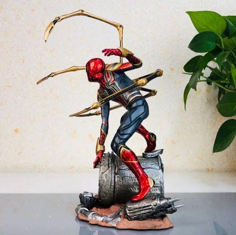 K&ouml;nnte beinhalten: Detaillierte Figur von Spider-Man in dynamischer Pose, mit rotem und goldenem Helm und Anzug mit blauen Akzenten. Die Figur ist auf einem strukturierten Metallsockel mit goldenen mechanischen Armen befestigt.