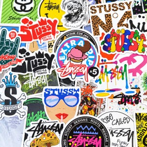 Puede incluir: Una colección de pegatinas de vinilo variadas con diversos diseños gráficos, incluyendo el logotipo de Stussy, un cono de helado, una cara con gafas de sol azules, setas y letras coloridas, todo superpuesto en un denso collage.