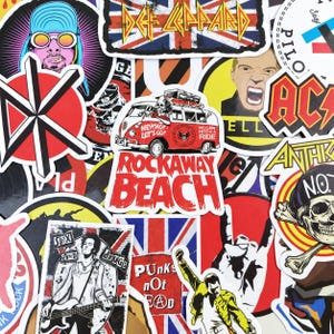Può includere: Una collezione di adesivi a tema musicale con vari loghi di gruppi rock, musicisti iconici e illustrazioni grafiche. Gli adesivi mostrano colori vivaci, una tipografia audace e immagini che includono un furgone rosso, teschi e motivi Union Jack.