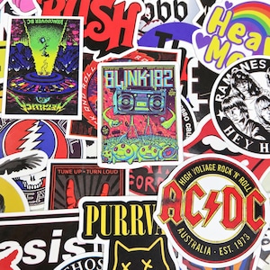 Op de afbeelding: Een verzameling muziekstickers met diverse bandlogo's en grafische illustraties, waaronder een AC/DC-embleem, een Blink-182 concertposter, een Metallica-afbeelding, een Ramones-portret en tekst zoals Tune Up Turn Loud.