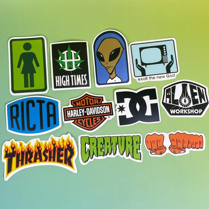 May include: A collection of colorful stickers with various designs. Includes a green and white sign with a stick figure, a black and green cannabis leaf, an alien, and a television with the text "exalt the new God". Other stickers feature the text "RICTA", "Harley-Davidson", "DC", "Alien Workshop", "Thrasher", "Creature", and "Toy Machine".