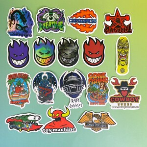 May include: A collection of colorful stickers with various designs. The stickers feature images of a woman, a creature, flames, a star, a skateboard, and a smiling face. Some stickers have text, including "THRASHER" and "COWBOY TUNED."