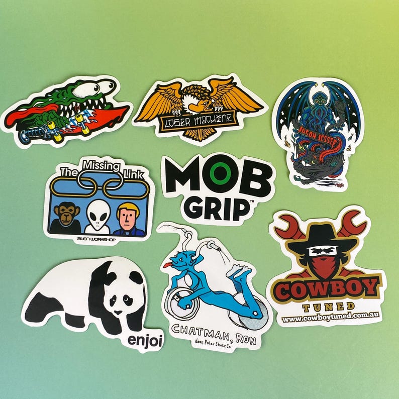 May include: A collection of colorful stickers with various designs. Included are stickers with an alligator on a skateboard, an eagle, a monster with wings, a panda, and the text "MOB GRIP". The stickers are on a green background.