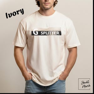 Peut inclure: T-shirt de couleur ivoire avec l'inscription "G Splitter" dans un rectangle noir et blanc. Le t-shirt est un modèle à col rond et est porté par une personne. Les mots "Shedit Merch" sont dans le coin inférieur droit.