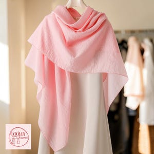 May include: A light pink scarf with a textured, semi-sheer fabric draped over a white garment. The scarf features a soft, flowing silhouette and is displayed on a hanger. A logo with the text LOOMA Scarves is visible in the bottom corner.