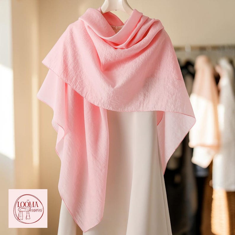 May include: A light pink scarf with a textured, semi-sheer fabric draped over a white garment. The scarf features a soft, flowing silhouette and is displayed on a hanger. A logo with the text LOOMA Scarves is visible in the bottom corner.