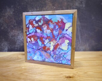Könnte beinhalten: Quadratisches abstraktes Gemälde in einem Holzrahmen. Das Kunstwerk zeigt eine farbenfrohe Komposition mit roten, lila und gelben Formen auf blauem Hintergrund. Der Rahmen besteht aus hellem Holz, und das Gemälde wird auf einer Holzoberfläche ausgestellt.