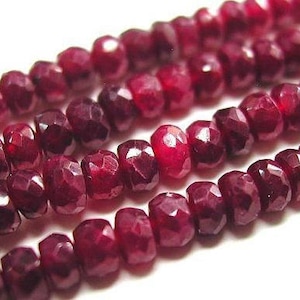 May include: A strand of deep red ruby beads, each bead is faceted and has a slightly irregular shape. The beads are strung together on a clear thread.