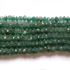 May include: Strands of faceted, emerald green gemstone beads. The beads are small, with a slightly irregular shape, and are strung together. The beads have a translucent quality, allowing light to pass through. The background is plain white.