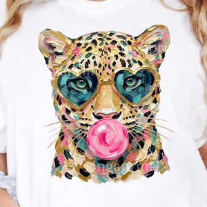 May include: White t-shirt with a leopard design. The leopard has heart-shaped sunglasses and a pink bubble. The illustration uses gold, teal, and pink colours. The shirt is labelled "PNG COMMERCIAL USE".