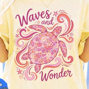 Könnte beinhalten: Hellgelbes T-Shirt mit einem rosa-korallenfarbenen Meeresschildkröten-Design und den Worten "Waves and Wonder". Die Schildkröte ist mit Muscheln und floralen Mustern verziert. Das T-Shirt hat eine lockere Passform.